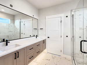 Full bath featuring a marble finish shower, double vanity, and light marble finish floors