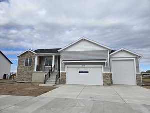 View of front of house featuring stone siding, driveway, covered porch, and a garage