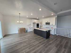 Kitchen with white cabinetry, a center island with sink, open floor plan, recessed lighting, and dark wood finished floors