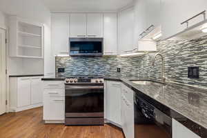 Kitchen with stainless steel appliances, white cabinetry, backsplash, open shelves, and dark wood finished floors