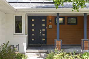 Doorway to property with solar panels, covered porch, roof with shingles, and brick siding