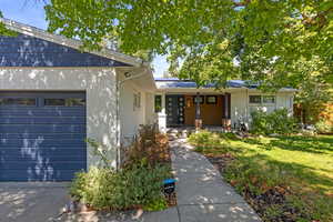 View of front of property featuring brick siding, covered porch, roof mounted solar panels, and an attached garage