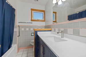 Bathroom with tile walls, light tile patterned flooring, wainscoting, vanity, and shower / tub combo with curtain