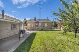 Rear view of property featuring a patio, a chimney, a lawn, and brick siding