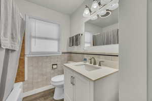 Full bath featuring vanity, tile walls, dark wood-type flooring, shower / bath combo, and a wainscoted wall