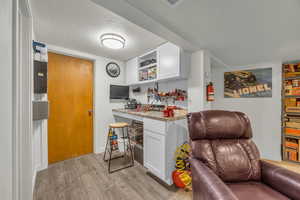 Bar featuring white cabinetry, a textured ceiling, light wood-style floors, light stone counters, and open shelves