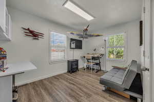 Home office with light wood-style floors, healthy amount of natural light, a wood stove, and a textured ceiling