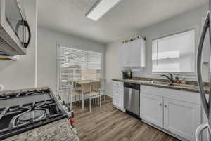 Kitchen with white cabinetry, a textured ceiling, appliances with stainless steel finishes, dark wood-style flooring, and plenty of natural light