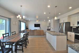 Kitchen featuring dark stone countertops, open floor plan, white cabinets, hanging light fixtures, and stainless steel appliances