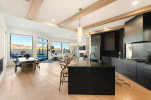 Kitchen with beam ceiling, modern cabinets, pendant lighting, a center island with sink, and dark cabinetry
