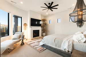 Carpeted bedroom with a ceiling fan, a lit fireplace, and recessed lighting
