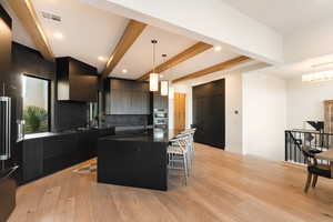 Kitchen with beamed ceiling, modern cabinets, an island with sink, dark cabinets, and a kitchen bar