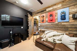 Carpeted living area featuring wooden walls and ceiling fan