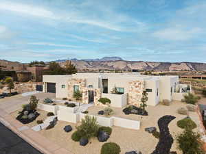 View of front of house featuring stucco siding, a fenced front yard, a mountain view, concrete driveway, and stone siding