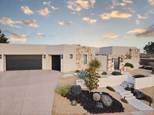 View of front facade featuring stucco siding, stone siding, a gate, and driveway