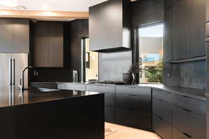 Kitchen with modern cabinets, dark cabinetry, stainless steel built in refrigerator, tasteful backsplash, and light wood-type flooring