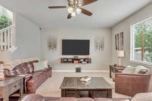 Living room featuring a ceiling fan, carpet, and stairway