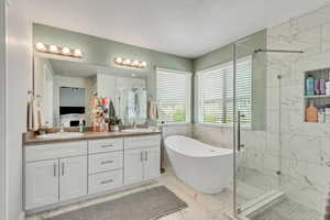 Bathroom featuring tile walls, a marble finish shower, light marble finish flooring, a freestanding tub, and double vanity