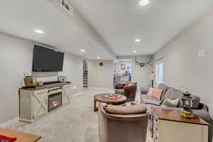 Living room with stairway, light carpet, recessed lighting, and a glass covered fireplace