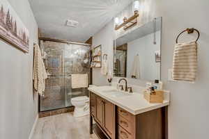 Bathroom with a textured ceiling, a stall shower, vanity, and light wood-style flooring