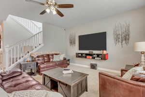 Carpeted living area with ceiling fan and stairway