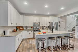 Kitchen featuring white cabinets, appliances with stainless steel finishes, light wood-style floors, a breakfast bar, and light stone countertops