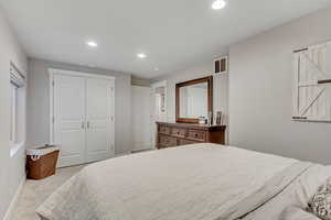 Bedroom with light colored carpet, recessed lighting, and a closet