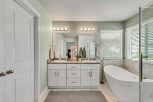 Full bath with a freestanding tub, double vanity, a shower stall, light marble finish floors, and tile walls