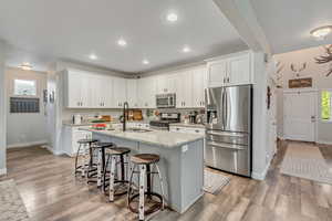 Kitchen featuring light stone counters, appliances with stainless steel finishes, a breakfast bar, a kitchen island with sink, and white cabinets