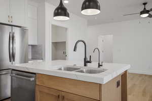 Kitchen with appliances with stainless steel finishes, light wood-type flooring, tasteful backsplash, hanging light fixtures, and light stone counters