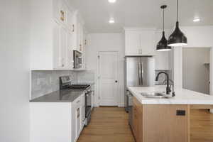 Kitchen with stainless steel appliances, decorative backsplash, white cabinets, pendant lighting, and an island with sink