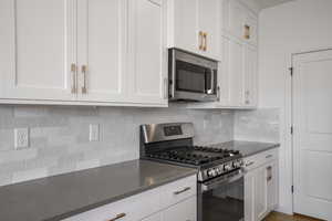 Kitchen featuring appliances with stainless steel finishes, white cabinetry, backsplash, and dark stone countertops