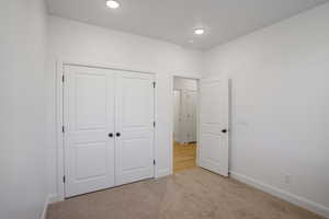 Unfurnished bedroom with light colored carpet, a closet, and recessed lighting