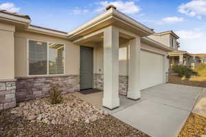View of exterior entry featuring stucco siding, stone siding, an attached garage, and concrete driveway
