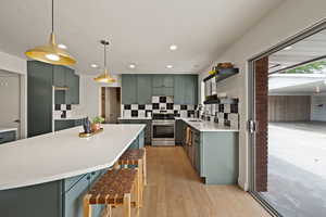 Kitchen featuring backsplash, green cabinets, light wood-style floors, stainless steel appliances, and pendant lighting