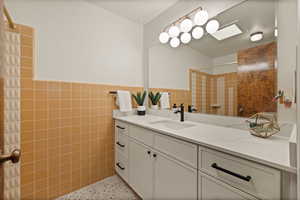 Bathroom featuring dark speckled floor, tile walls, a tile shower, vanity, and a wainscoted wall