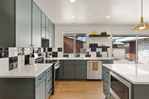 Kitchen featuring appliances with stainless steel finishes, recessed lighting, tasteful backsplash, light wood-style floors, and decorative light fixtures