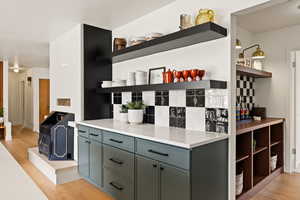 Bar area featuring open shelves, light wood-style floors, decorative backsplash, a wood stove, and light stone counters