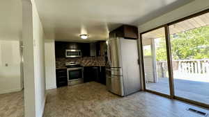 Kitchen featuring appliances with stainless steel finishes, decorative backsplash, dark cabinetry, and dark countertops