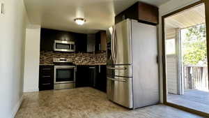 Kitchen with appliances with stainless steel finishes, backsplash, and dark cabinetry