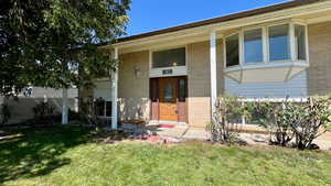 View of exterior entry featuring brick siding, a lawn, and covered porch