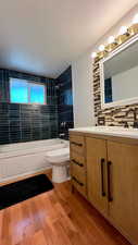 Bathroom with shower / tub combination, vanity, light wood finished floors, and tasteful backsplash