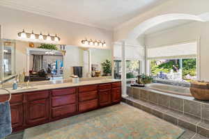 Ensuite bathroom with a garden tub, double vanity, crown molding, and a textured ceiling