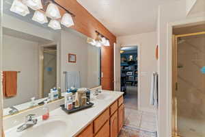 Full bath featuring double vanity, a stall shower, a textured ceiling, light tile patterned floors, and a chandelier