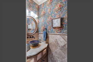 Half bath featuring vanity, wainscoting, tile walls, ornamental molding, and wallpapered walls