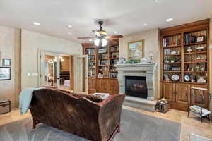 Living room with built in shelves, light tile patterned floors, a ceiling fan, a glass covered fireplace, and recessed lighting