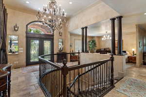 Entrance foyer featuring a chandelier, stone tile flooring, french doors, crown molding, and decorative columns