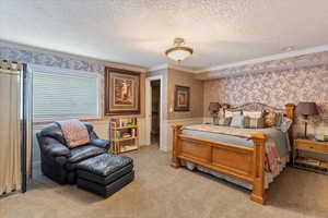 Carpeted bedroom featuring wallpapered walls, ornamental molding, a textured ceiling, and wainscoting,
