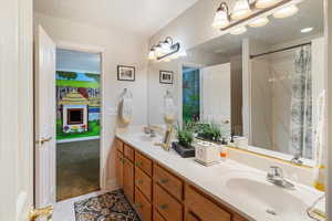 Full bath with a textured ceiling, double vanity, light tile patterned floors, and a shower with curtain