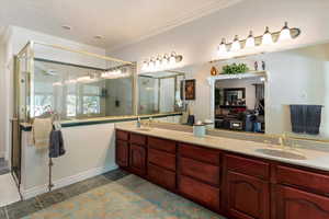 Bathroom with a stall shower, connected bathroom, double vanity, dark tile patterned floors, and crown molding